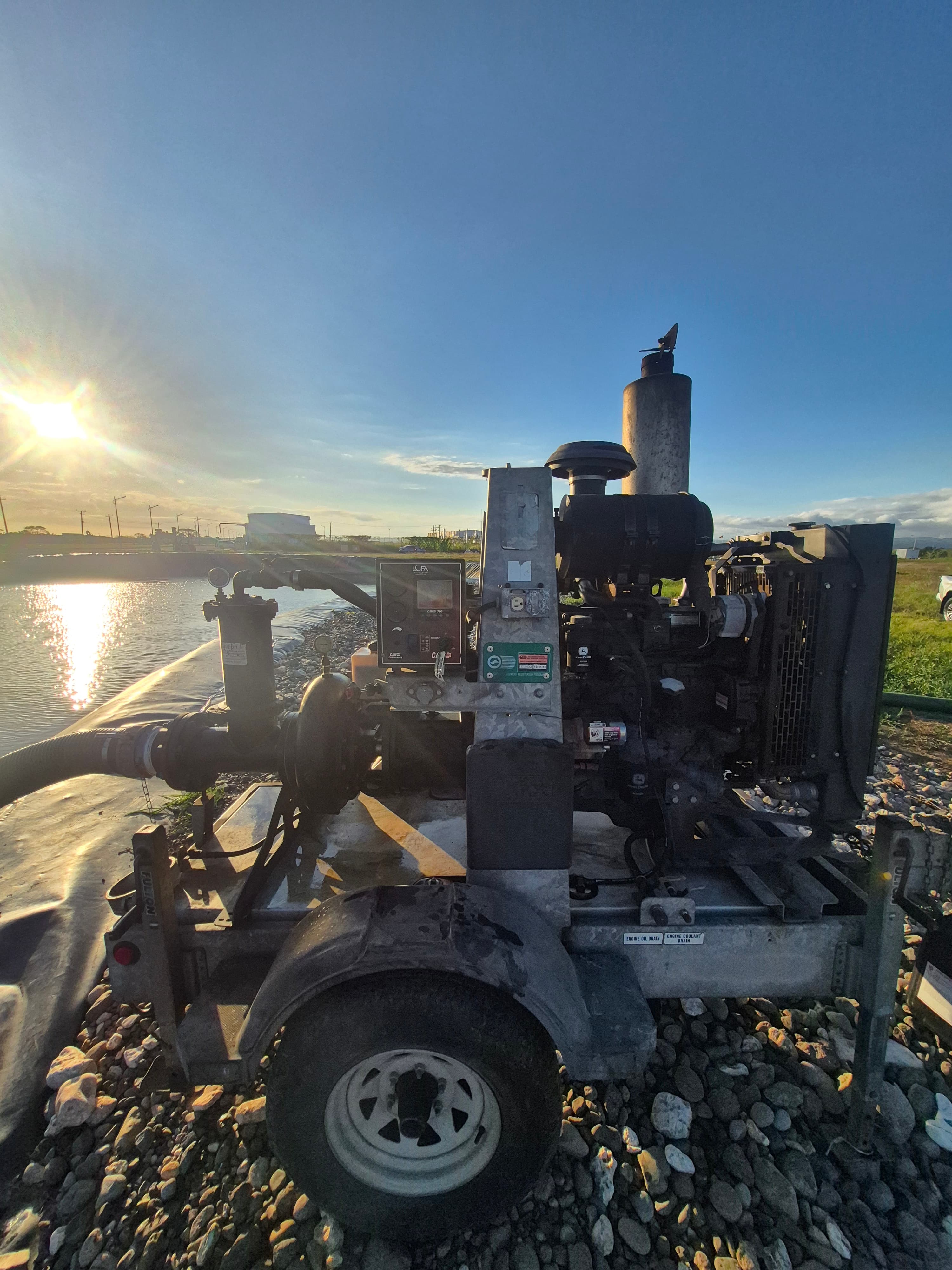 Diesel industrial pump on a trailer beside a reservoir under a bright sun.